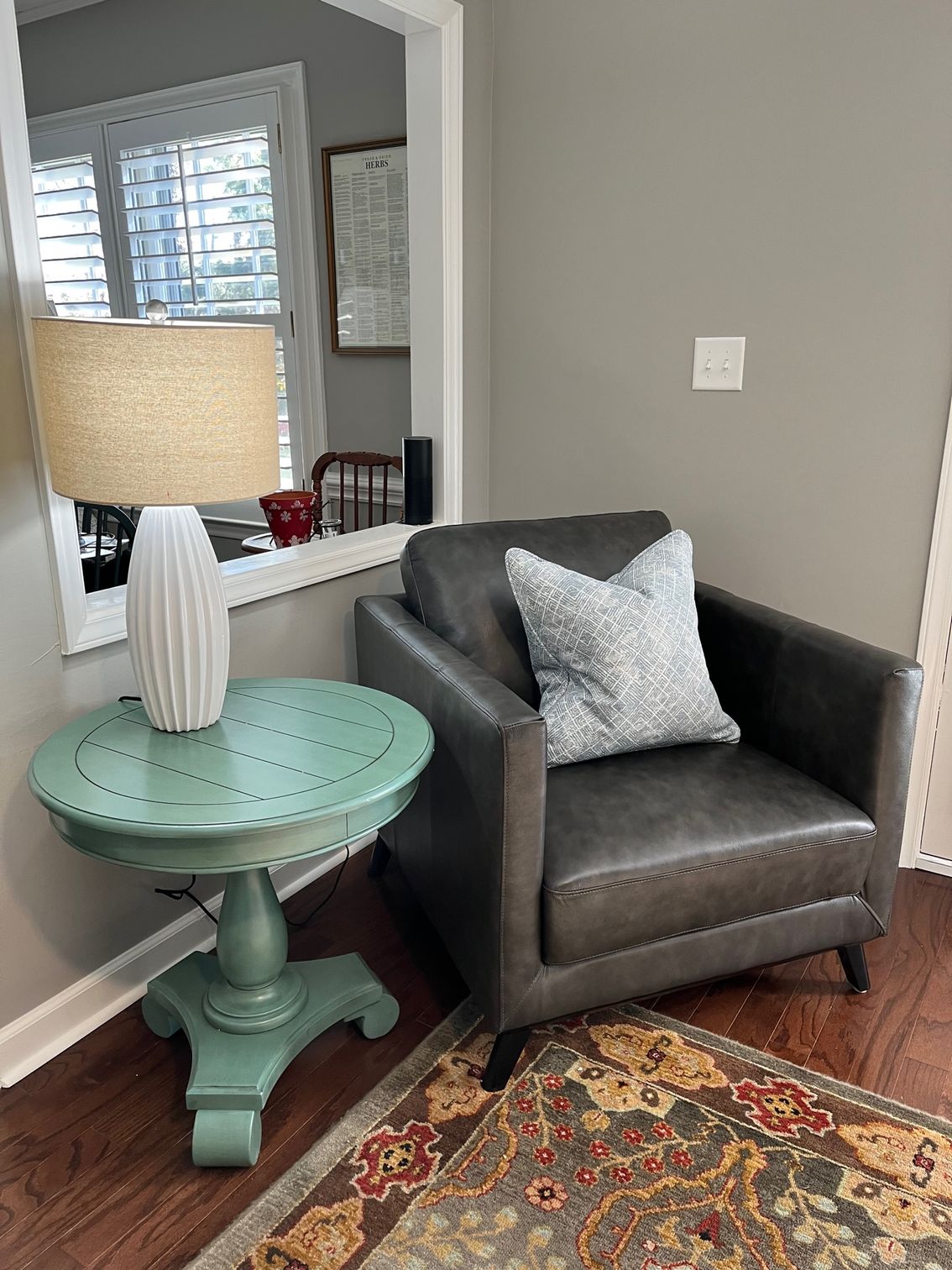 Gray armchair next to a teal side table with a lamp on it, set on an oriental rug.