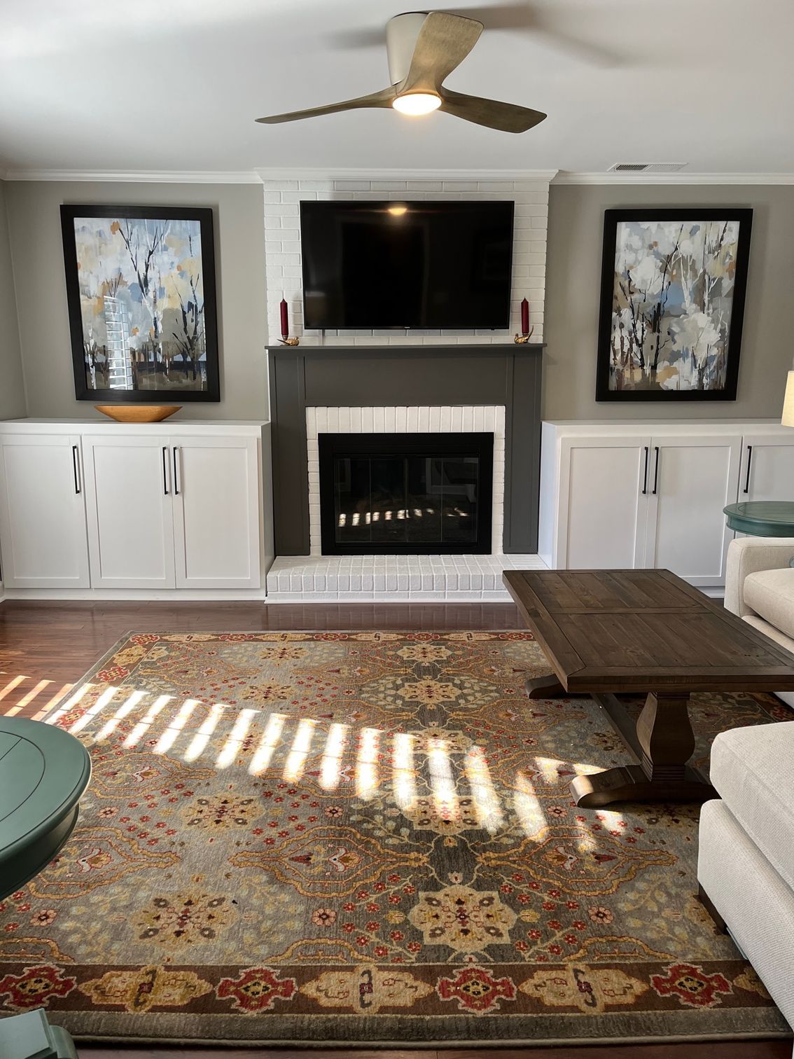 Living room with fireplace, TV, and art. White cabinets, gray walls, and a brown rug.