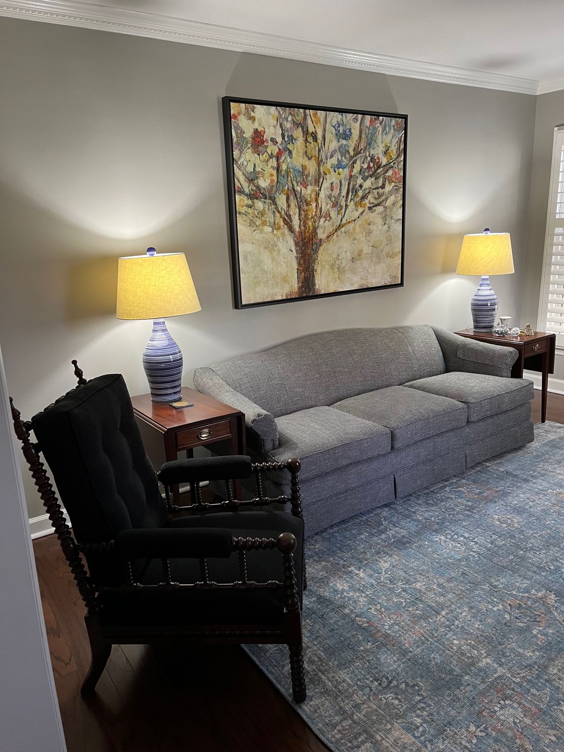 Living room with gray sofa, blue rug, dark armchair, and art.