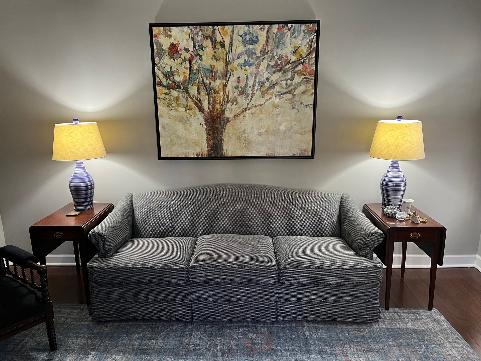 Sofa with lamps on each side and a tree painting above it; against a gray wall.