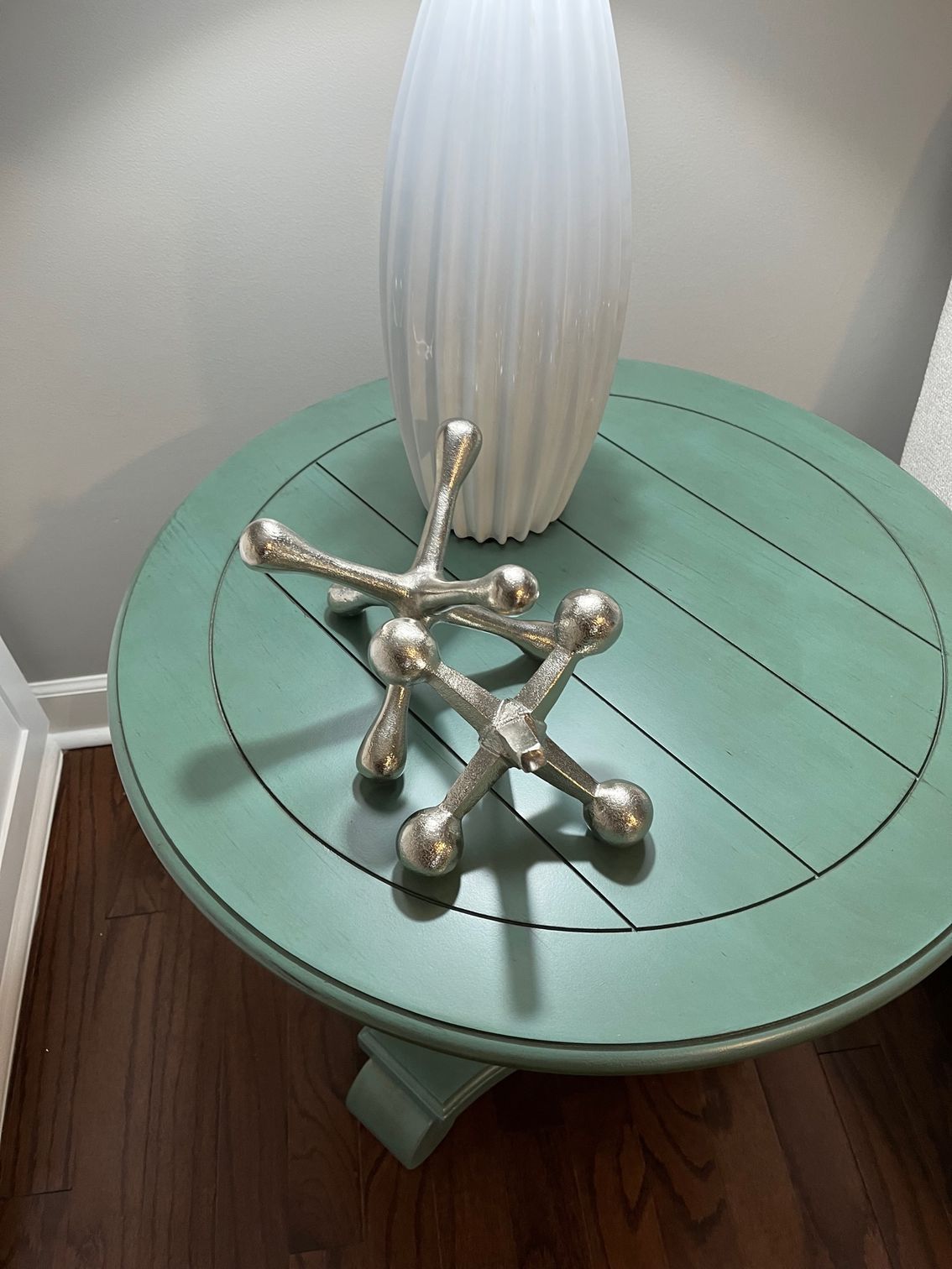 Two silver jack sculptures on a teal round table with a white vase.