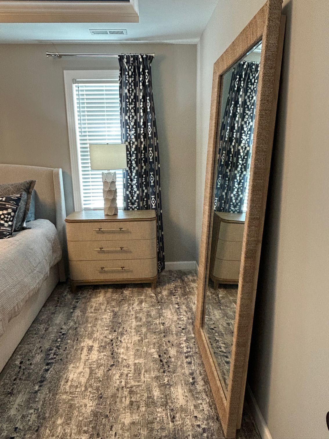 Large mirror leaning against a wall in a bedroom with a nightstand and patterned rug.
