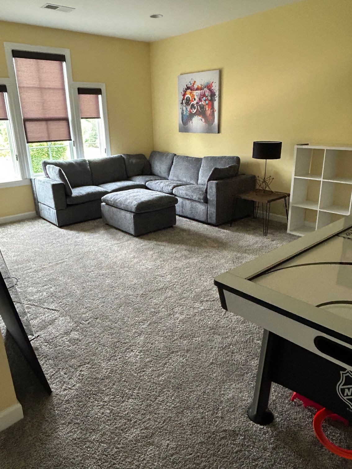 Gray sectional sofa and ottoman in a yellow-walled room with a foosball table and shelving.