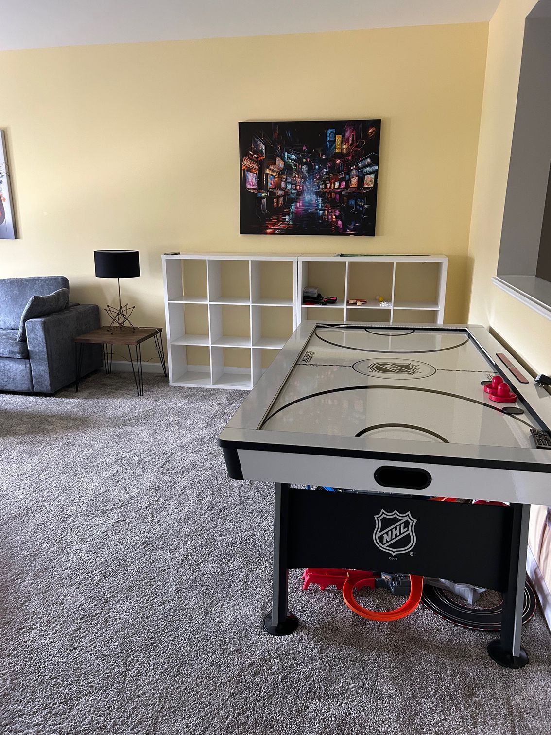 An air hockey table in a game room with cubby shelves, sofa, and art on the wall.