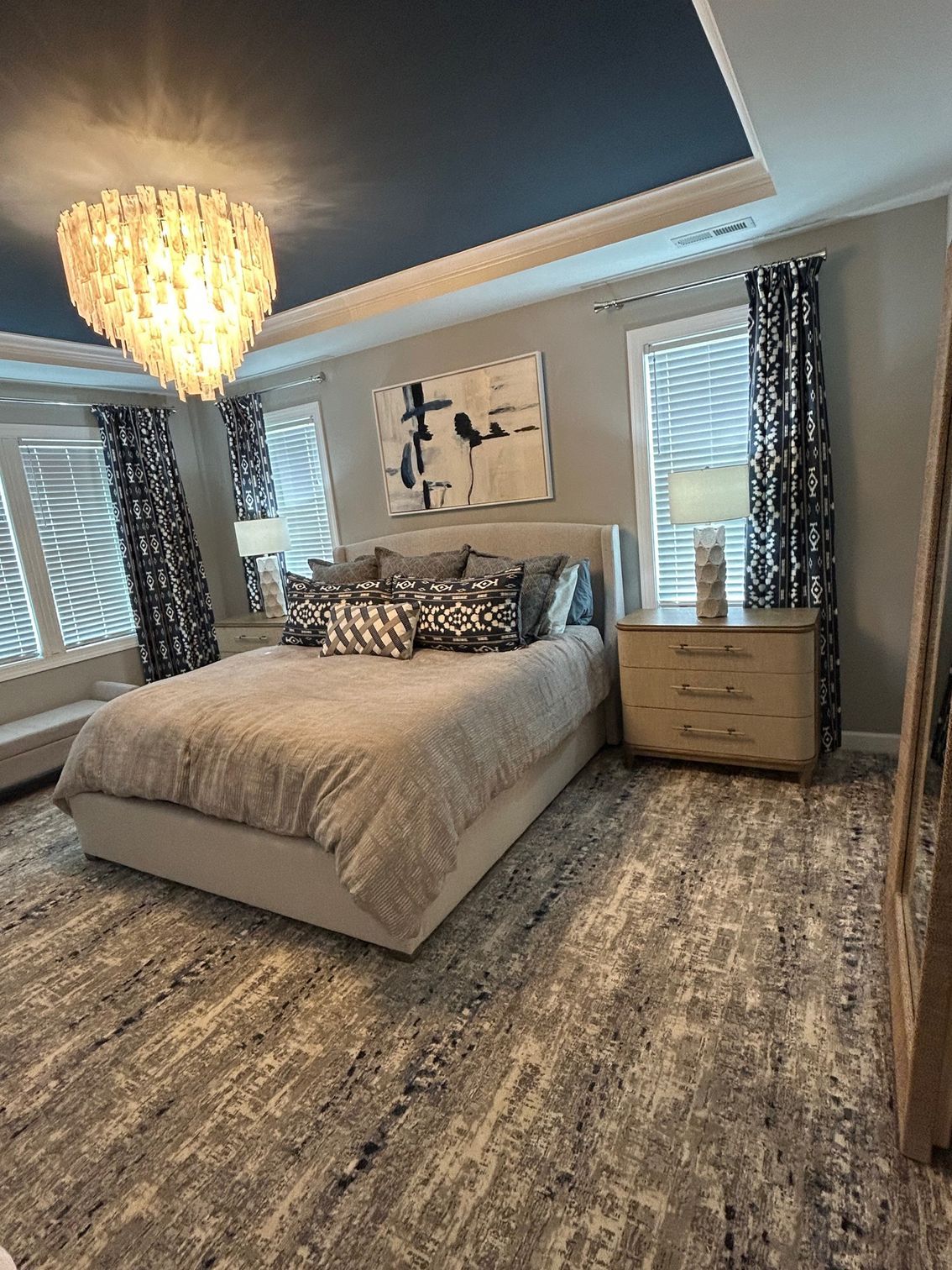 Bedroom with a gray bed, patterned rug, blue ceiling, chandelier, and patterned curtains.