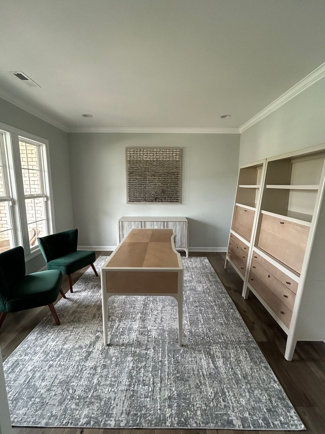 Office with desk, rug, bookshelves, chairs, and artwork against pale green walls.