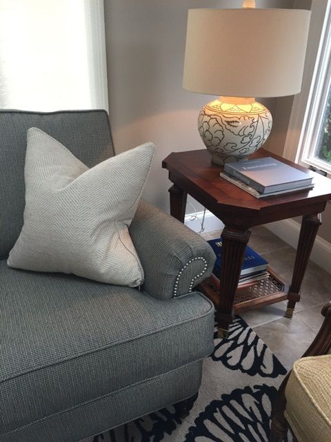 Blue armchair with patterned pillow next to a dark wood table with a lamp and books.