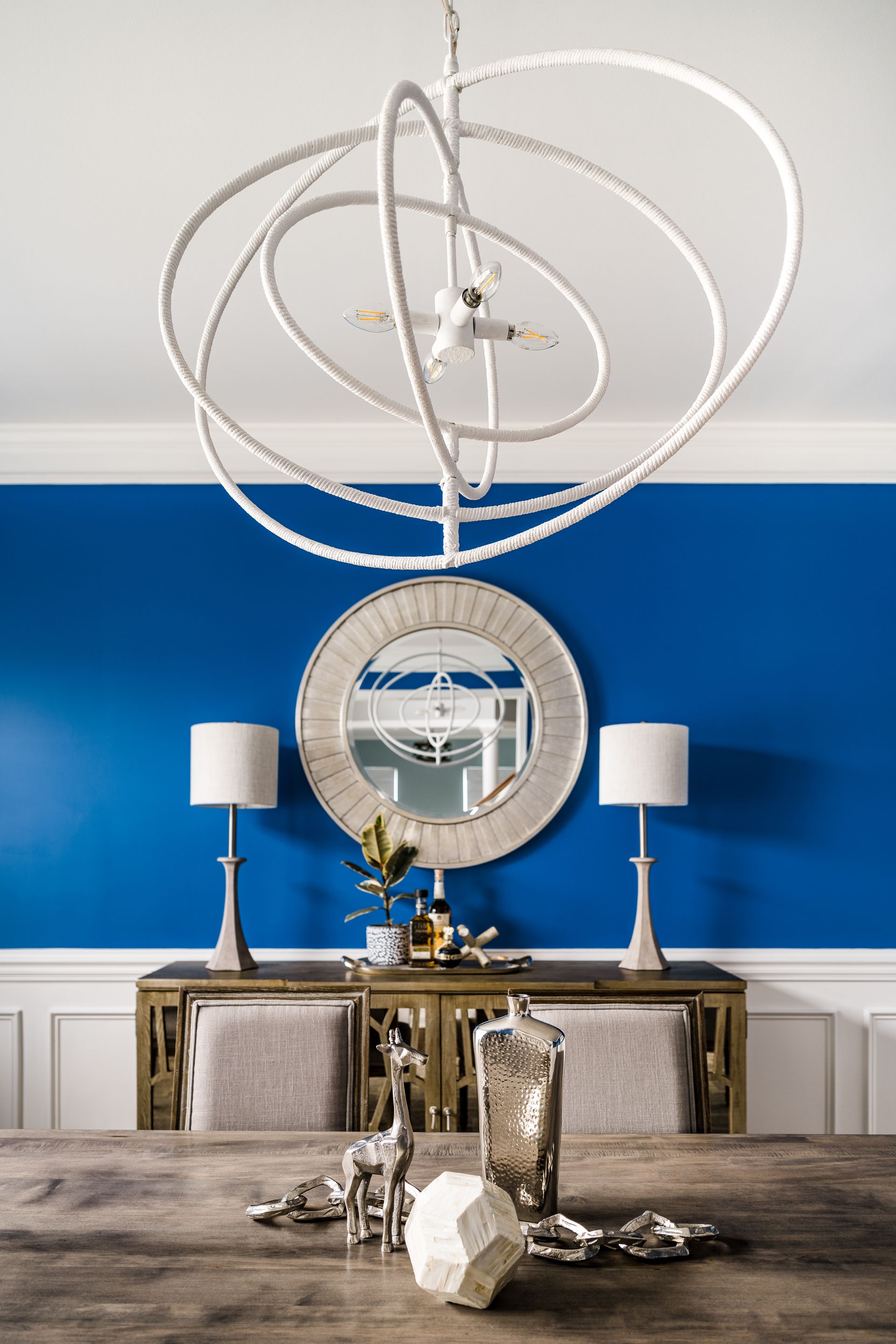 Dining room with blue wall, gold accents, ornate chandelier, table setting, and mirror.