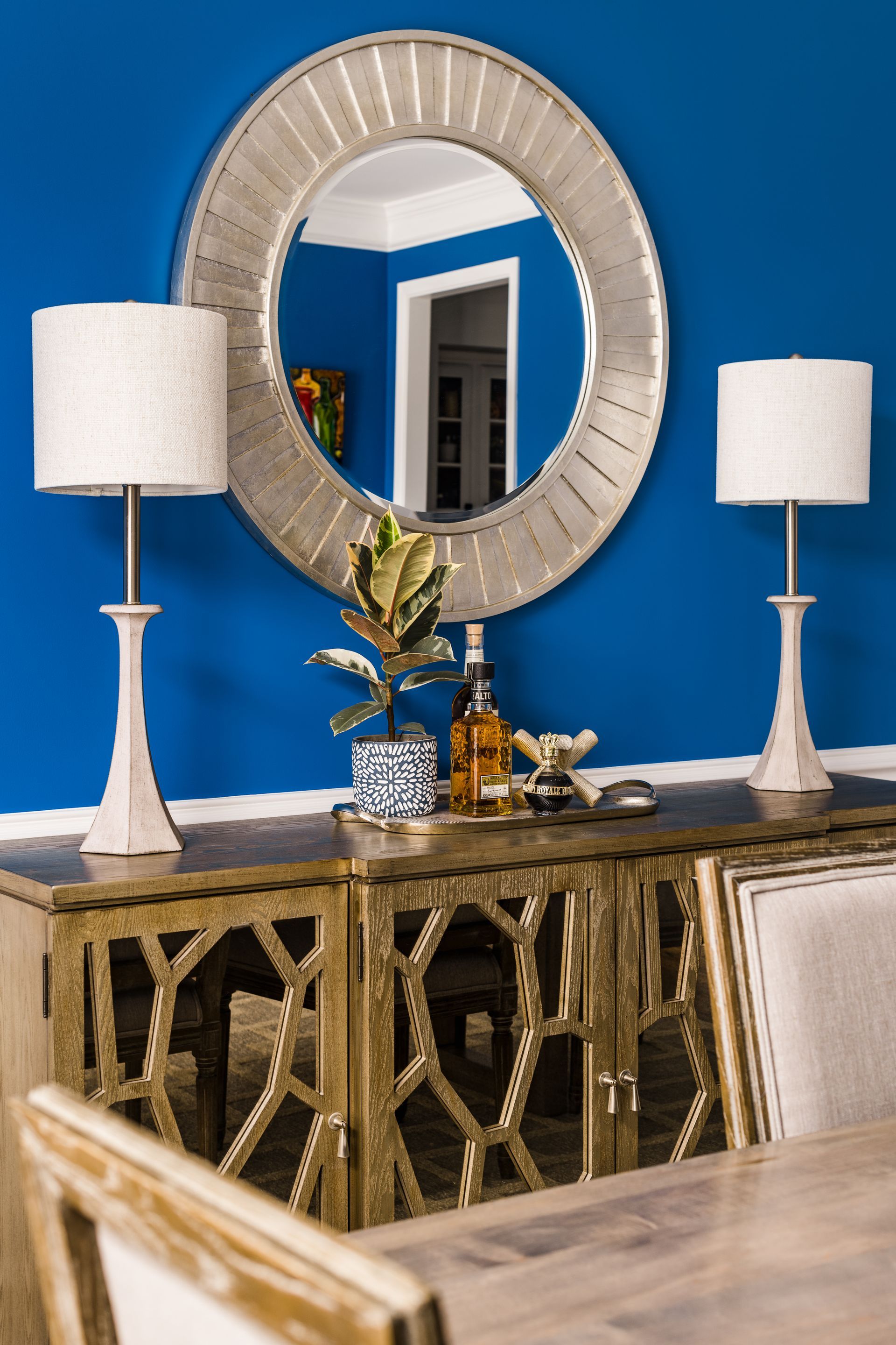Gold sideboard with lamps, mirror, and plant against a vibrant blue wall.
