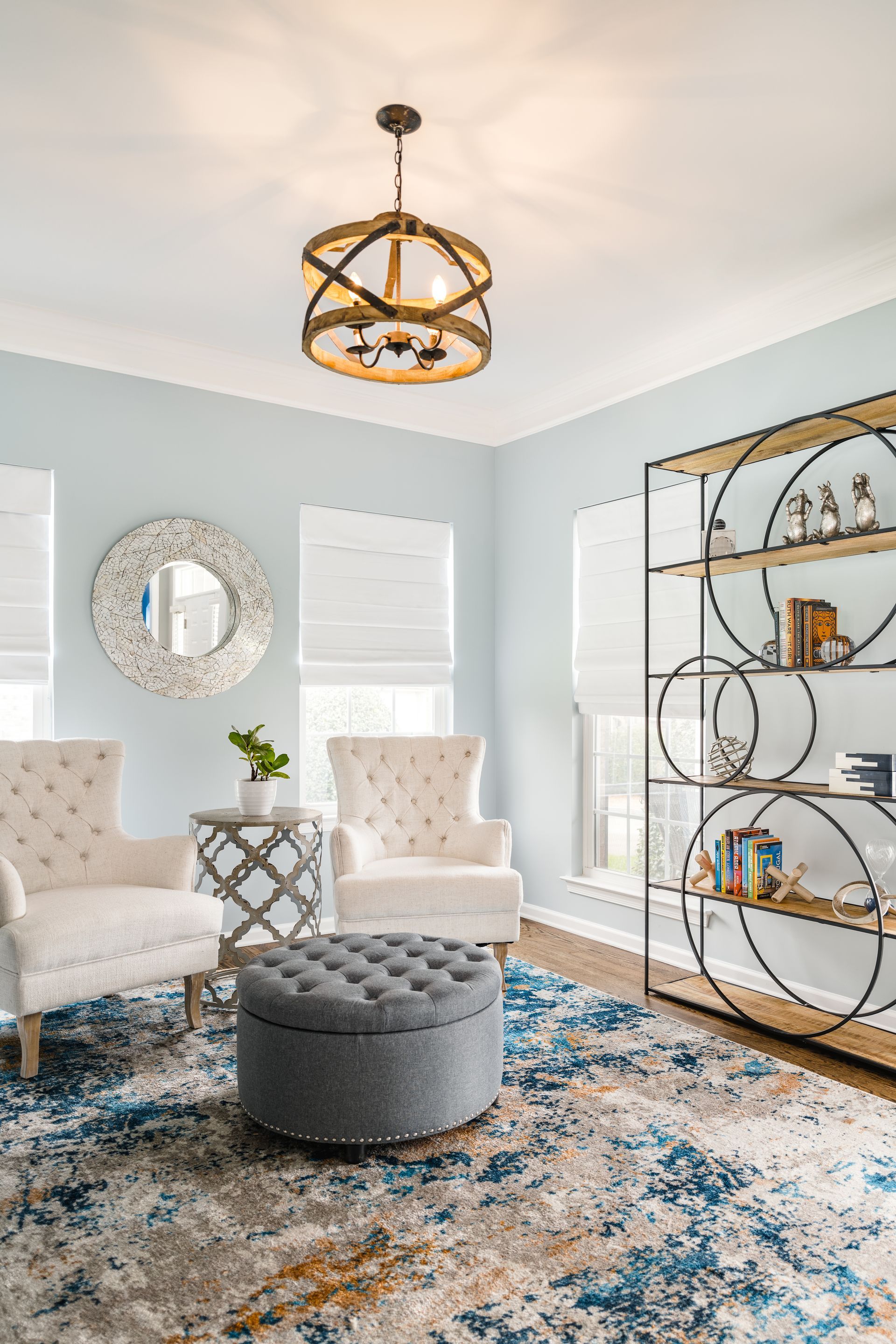 A light blue sitting room with two white chairs, a patterned rug, and a bookshelf.