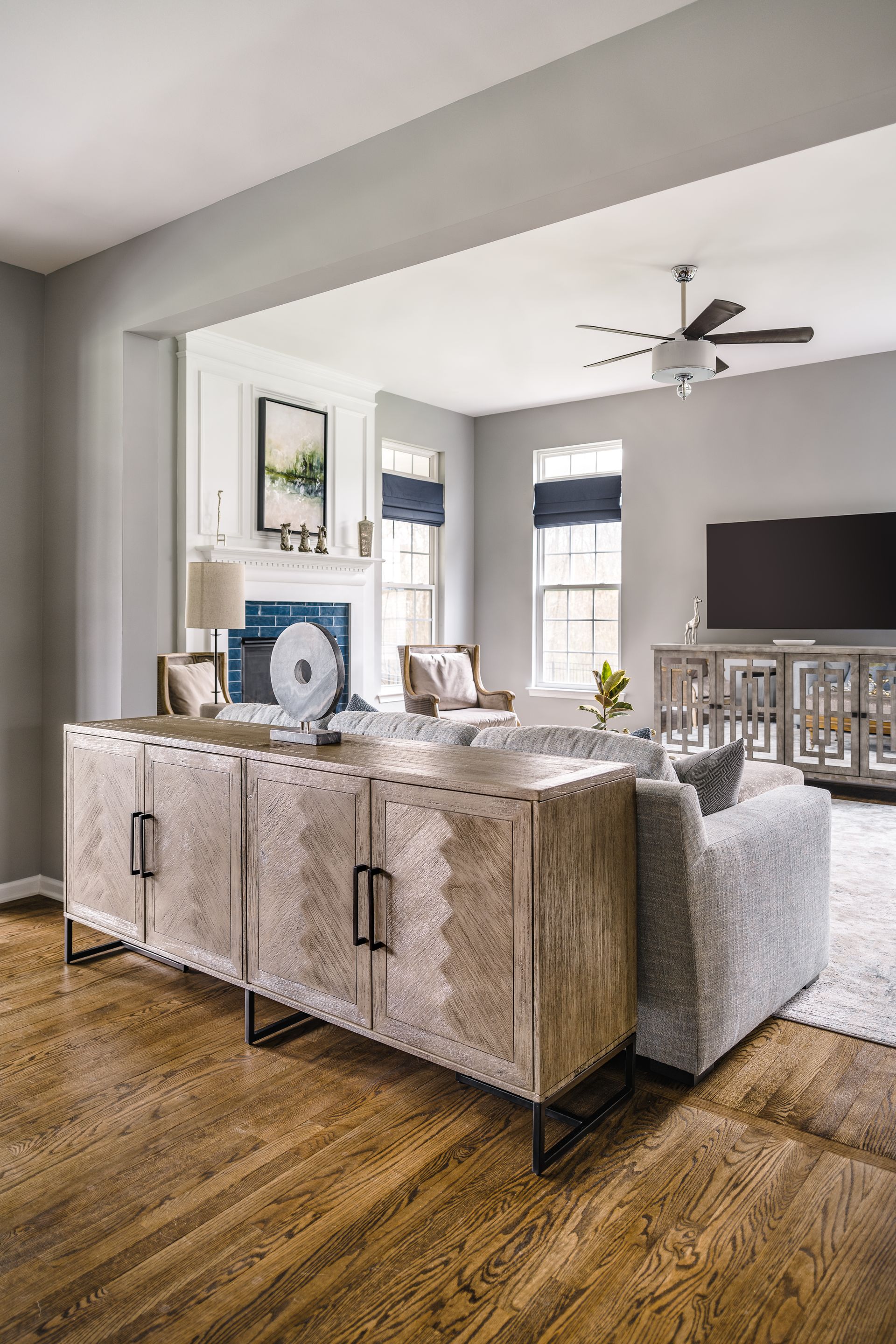 Living room with wooden sideboard, white fireplace, gray walls, and wood floors.