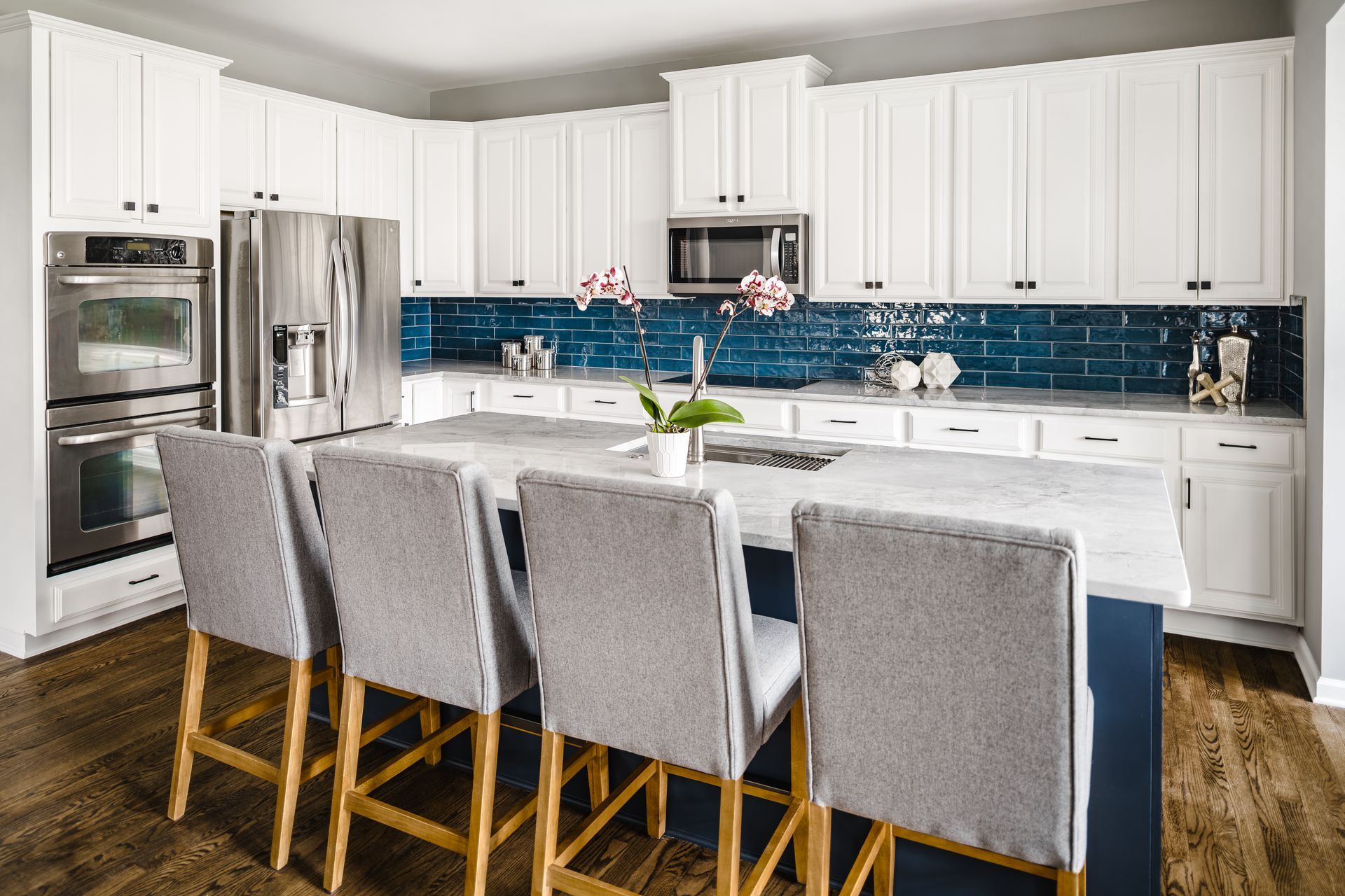 White kitchen with blue tile backsplash, large island with stools, stainless steel appliances.