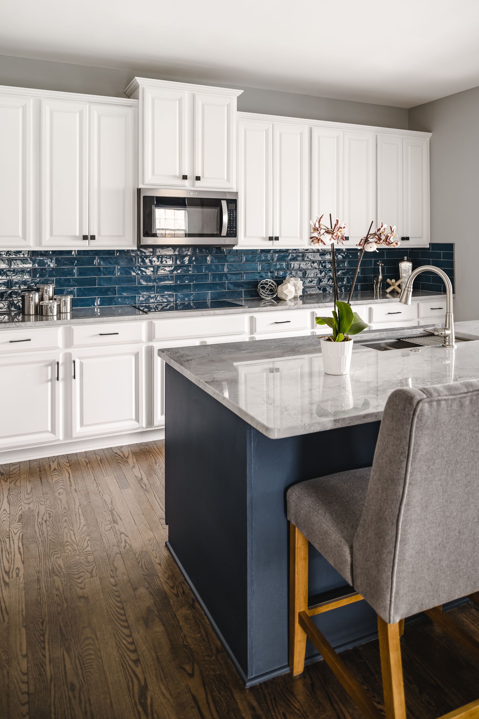 White kitchen with blue backsplash, navy island, and gray bar stools.