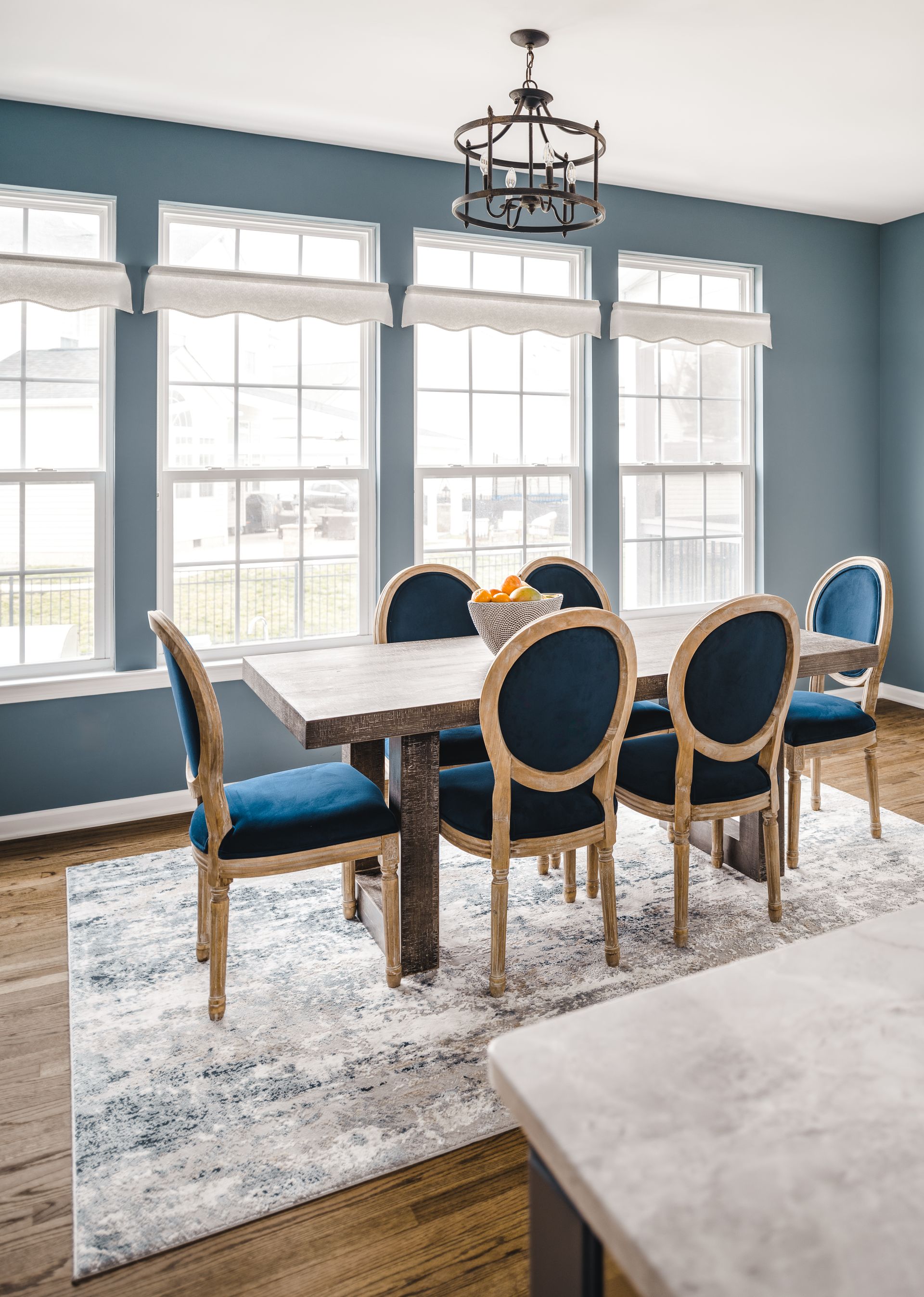 Dining room with blue walls, wood table and chairs, and area rug.