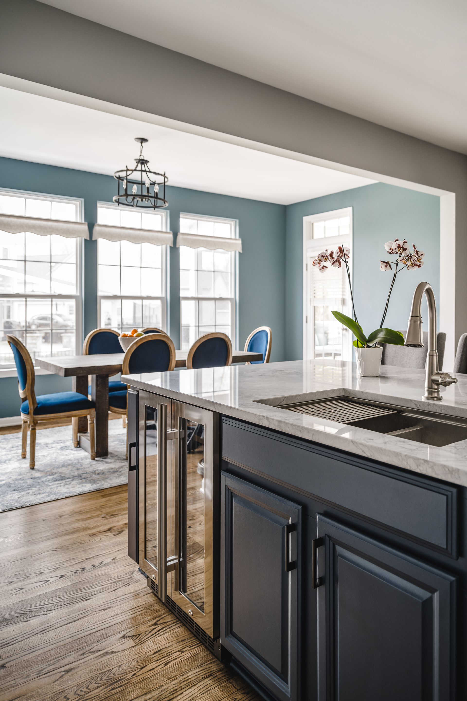 Kitchen with dark blue island and light wood floor, leading to a blue dining area with a table and chairs.