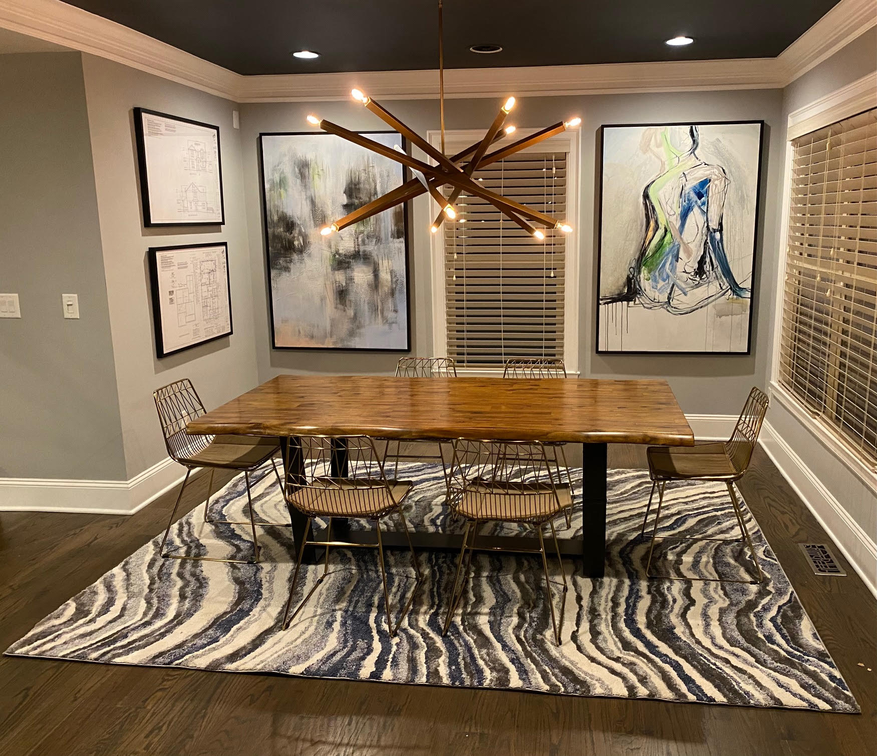 Dining room with a wooden table, abstract art, modern light fixture, and patterned rug.