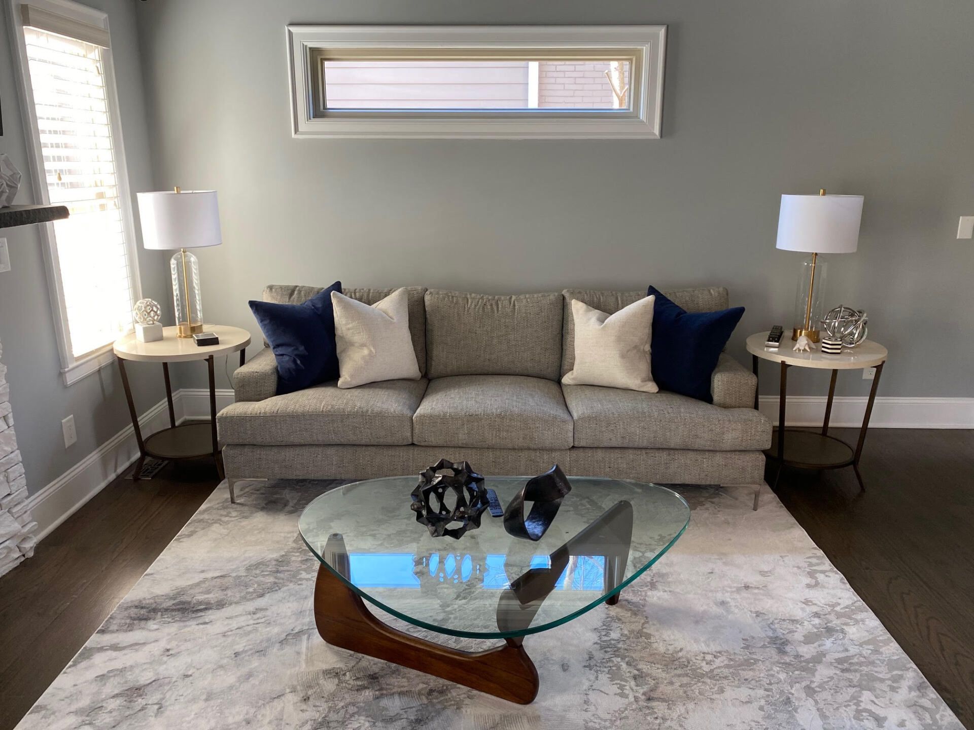 Living room with gray sofa, blue and cream pillows, round glass coffee table, and side tables with lamps.