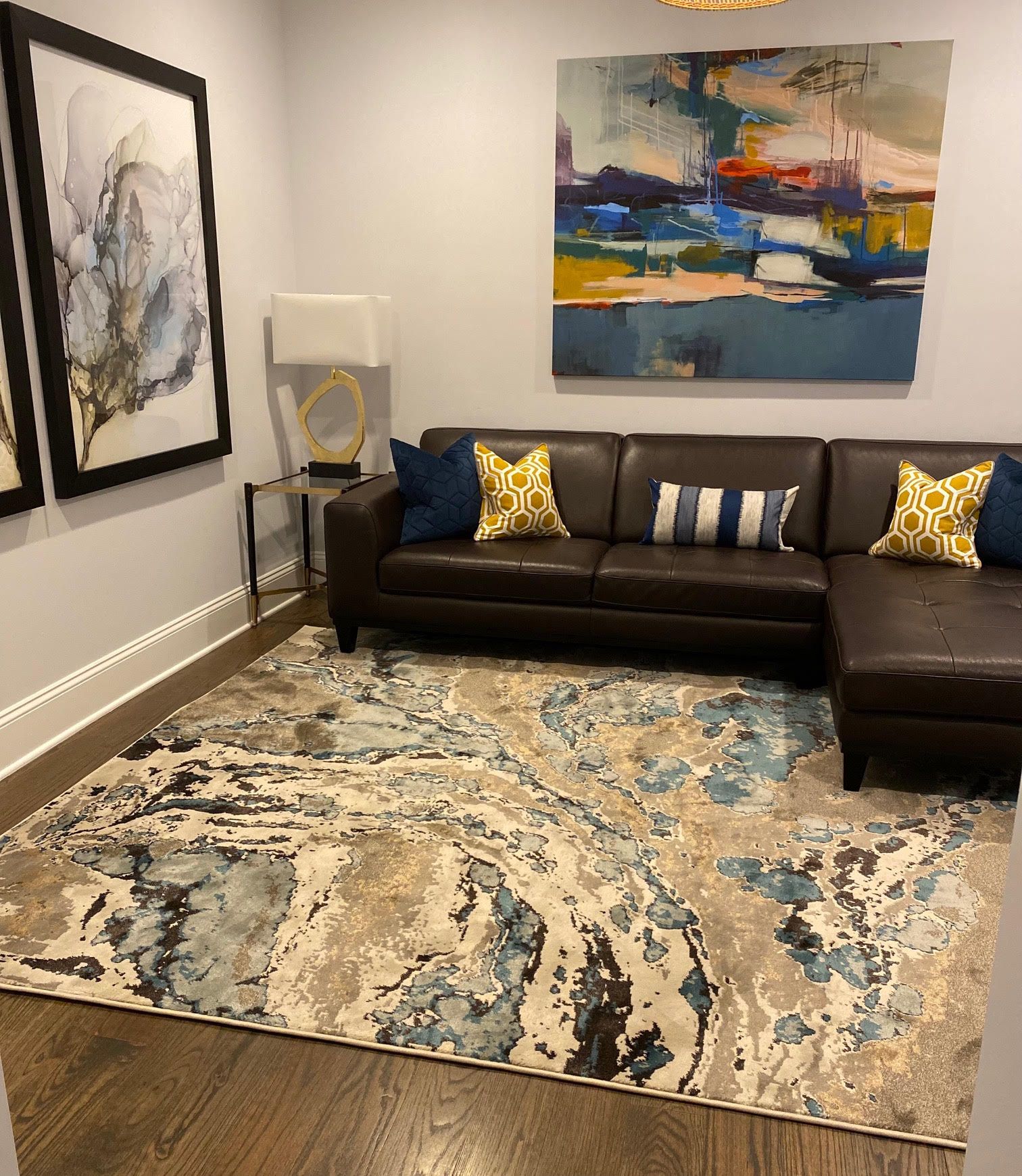Living room with a brown leather sectional, abstract rug, art, and pillows.