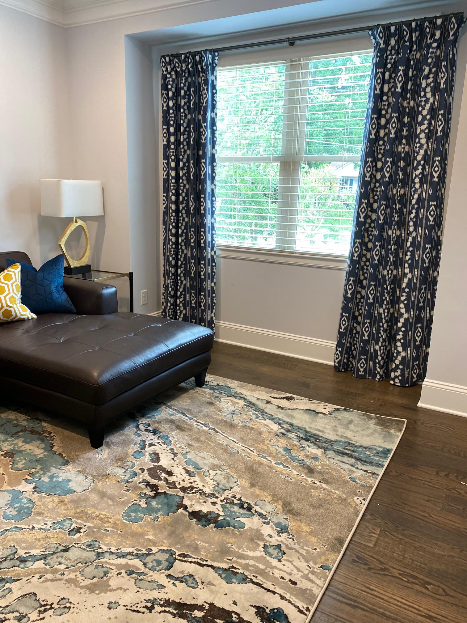 Living room with brown leather chaise lounge, patterned rug, navy curtains, and window with blinds.