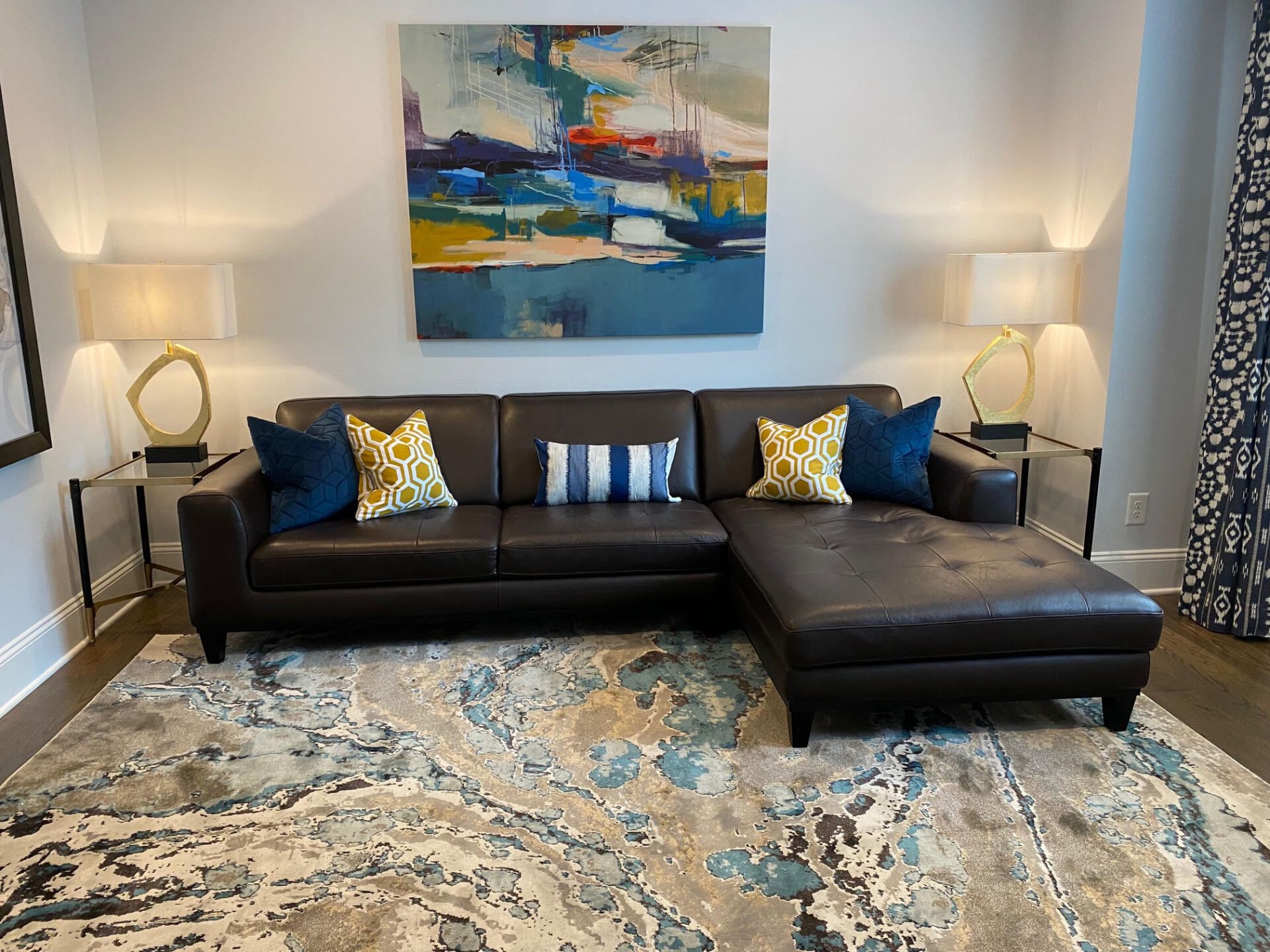 A living room with a brown sectional couch, abstract art, and a patterned rug.