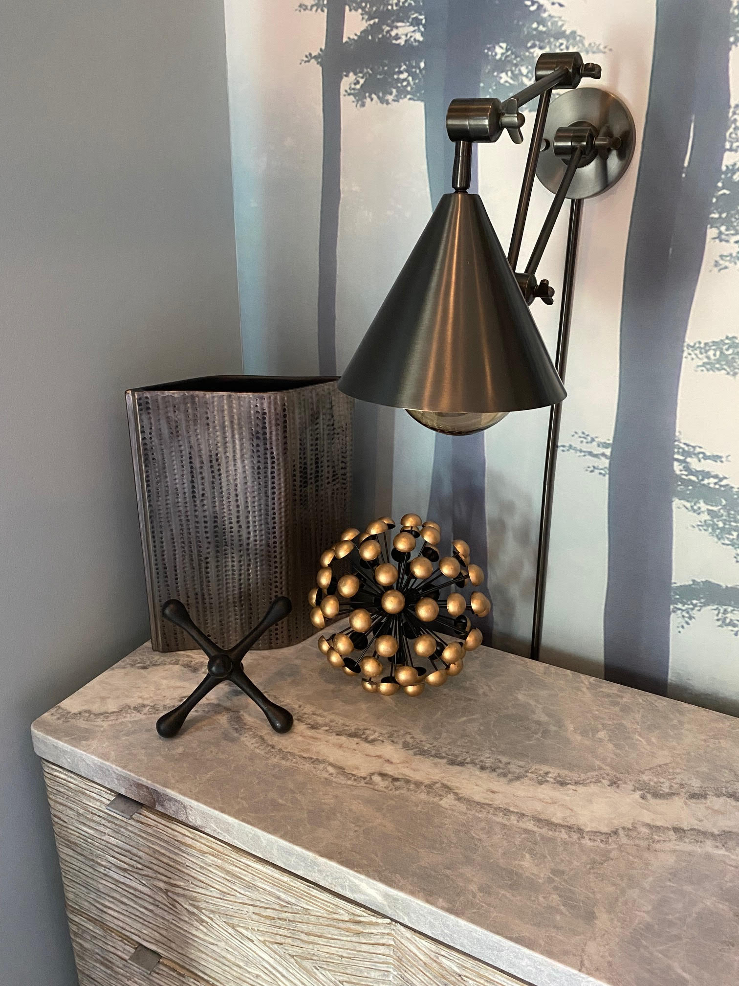 Corner shelf with decorative objects: trash can, jack, sphere, lamp. Wallpaper backdrop of silhouetted trees.