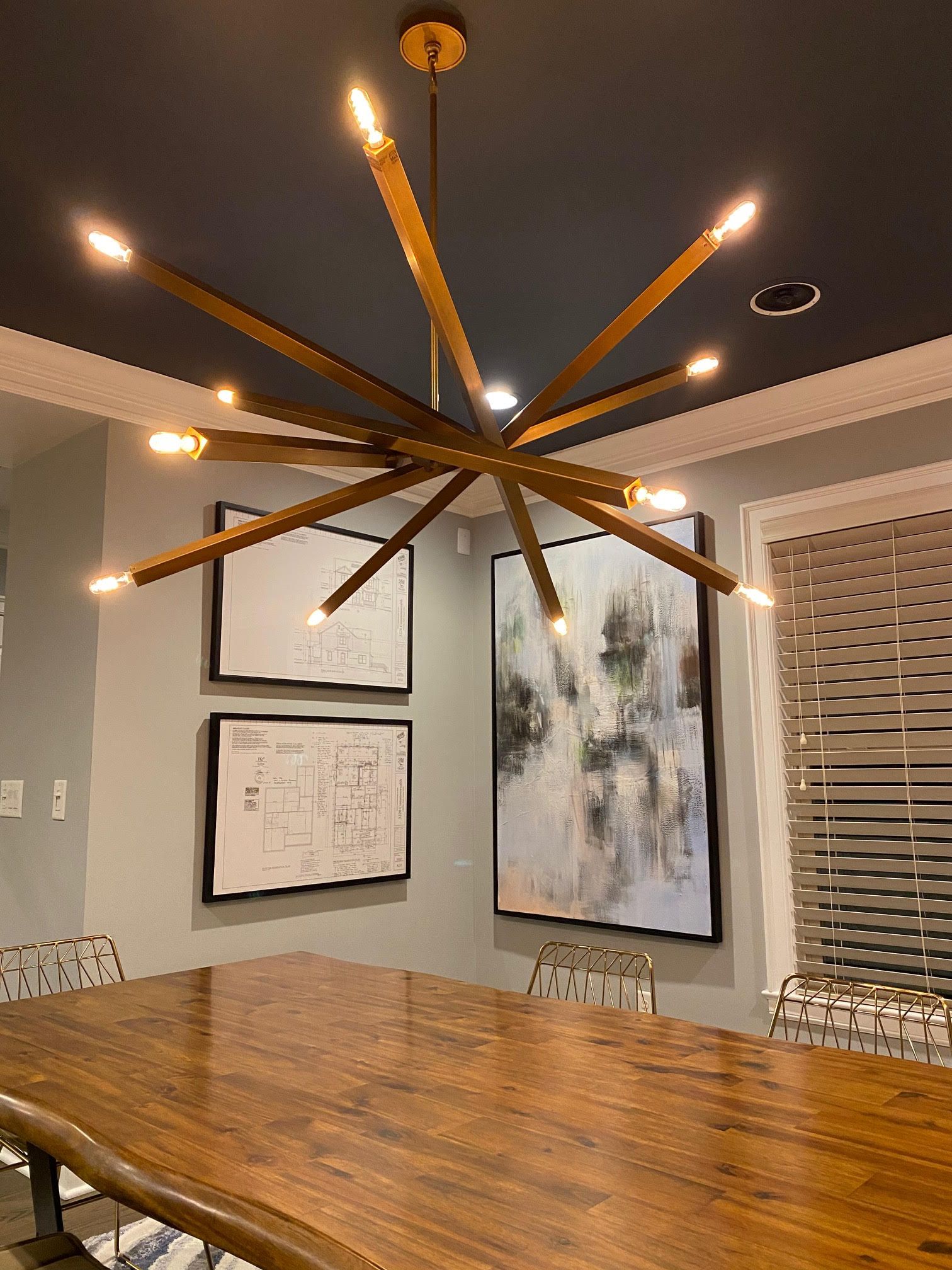 Dining room with a large wooden table, modern chandelier, and framed artwork.