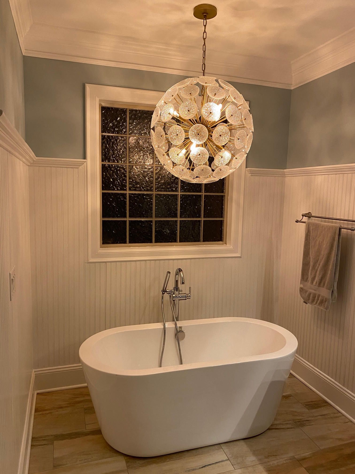 Bathroom with white soaking tub, crystal chandelier, blue walls, window, and towel rack.