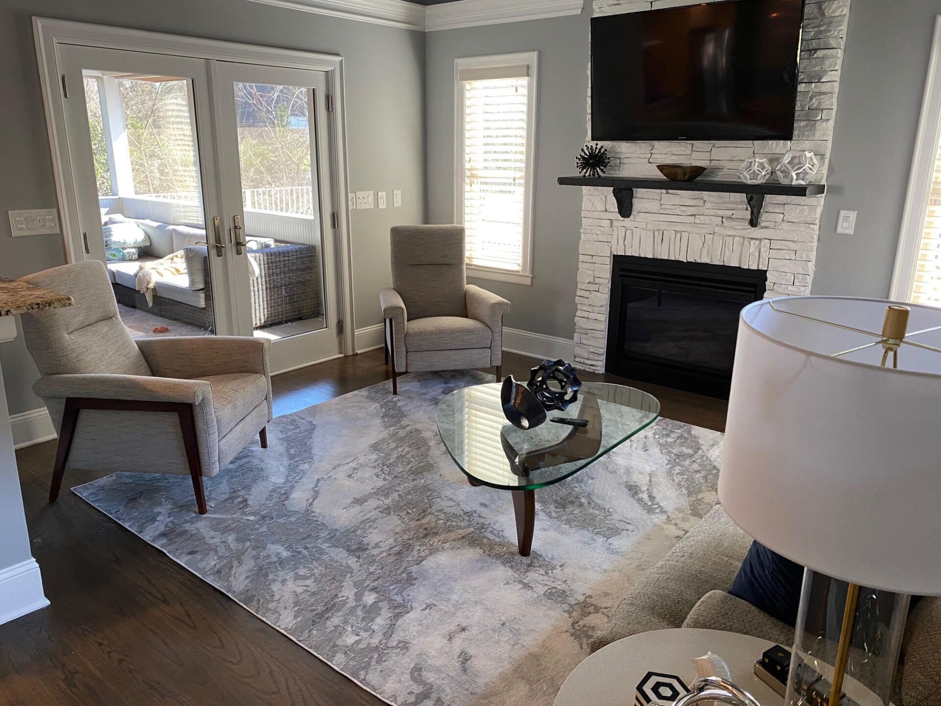 Living room with gray walls, chairs, fireplace, glass coffee table, and rug. French doors lead to a porch.