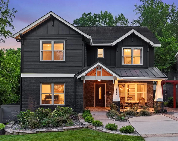 Two-story house with dark gray siding, brick porch, lit windows, and landscaping.
