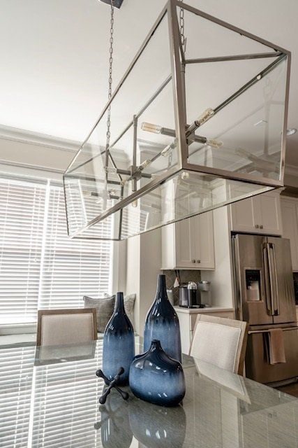 Dining room with a glass chandelier, granite table, blue vases, and stainless steel refrigerator.