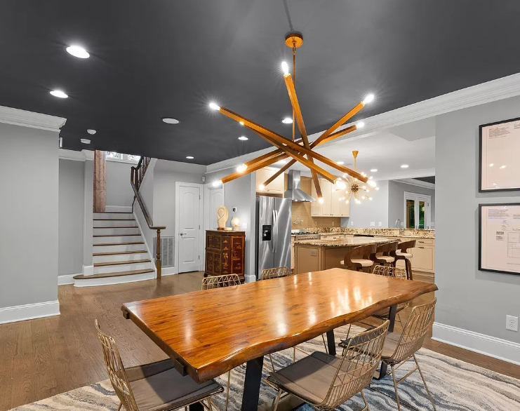 Dining room with wooden table, metal chairs, and modern chandelier under a dark gray ceiling.