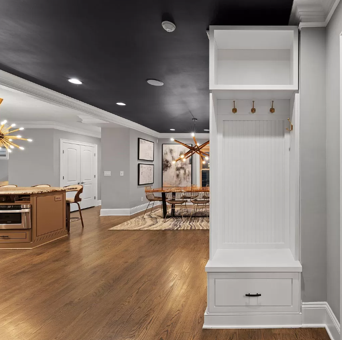 White built-in entryway unit with bench, hooks, and storage in a home with hardwood floors and dark ceiling.