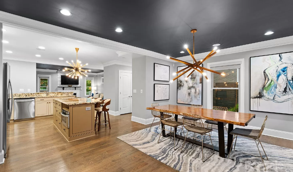 Modern dining area with a dark gray ceiling, wooden floor, and a long wooden table.