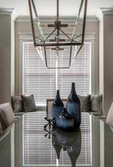 Dining table with blue vases, window seat with pillows, and a chandelier.