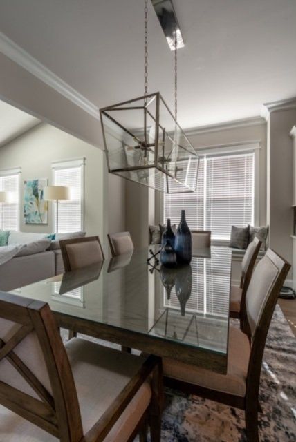 Dining room with a glass-top table and chairs.  A large light fixture hangs above.  Window seat in the background.