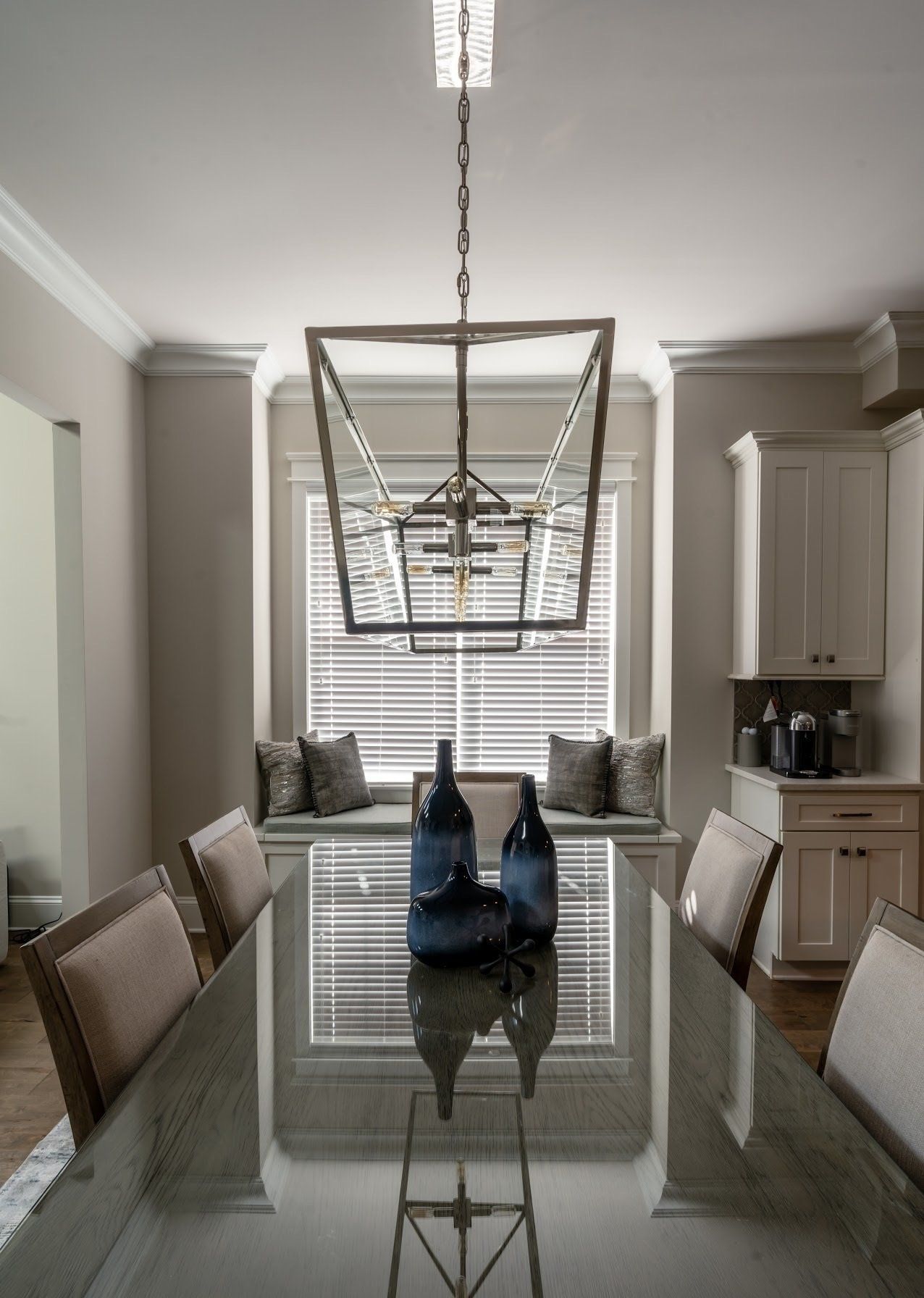 Dining room with rectangular table, chairs, and window seat, beneath a chandelier.