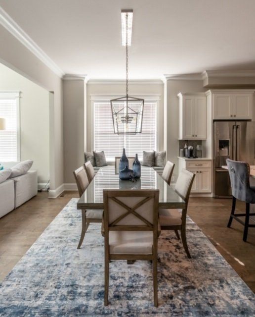 Dining room with table, chairs, and rug; window seat with pillows, blue accents, neutral walls.