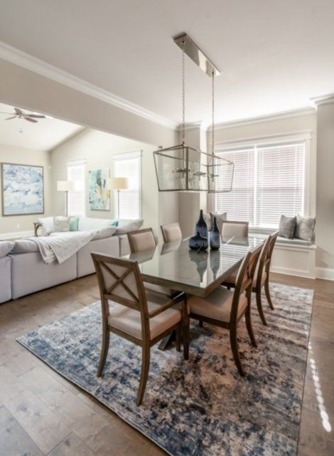 Dining room with table, chairs, rug, and chandelier, open to living room with sofa and art.
