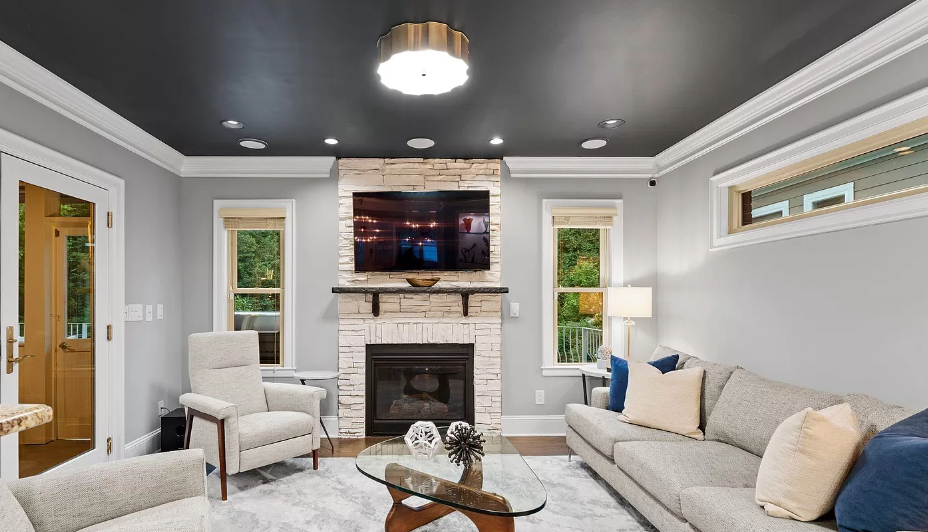 Living room with stone fireplace, TV, gray couch, chairs, and a black ceiling.