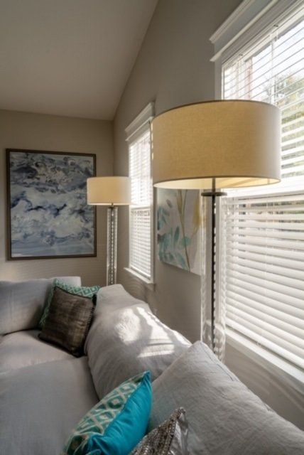 Living room with two tall lamps beside a couch, windows with blinds, and framed art on the wall.