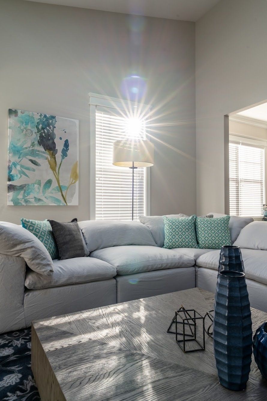 Bright living room with white sectional, large window, teal accents, and sunlight.