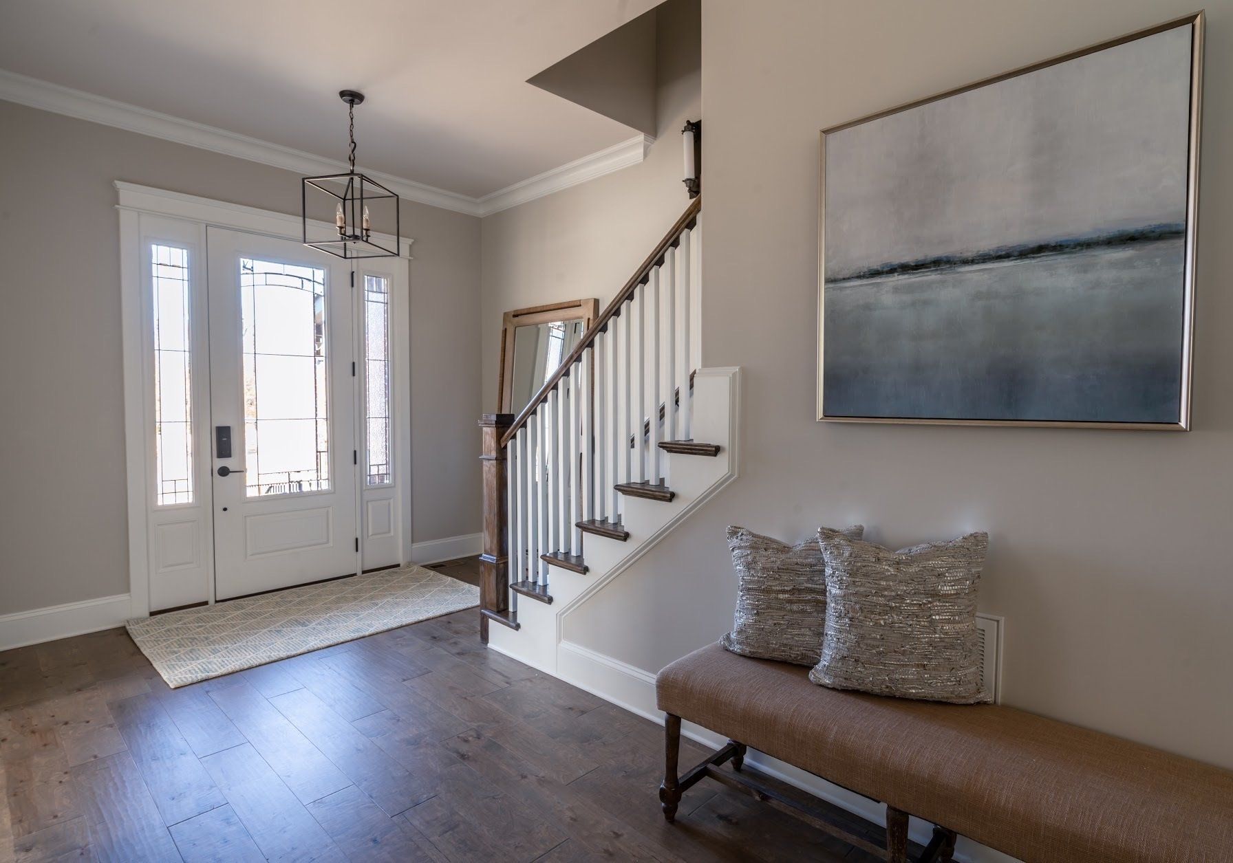 Entryway with white double doors, staircase, bench with pillows, artwork, and dark wood floor.
