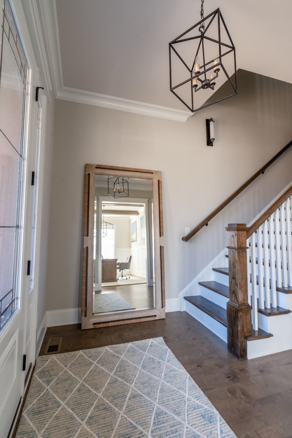 Entryway with a large mirror, staircase, patterned rug, and geometric chandelier.