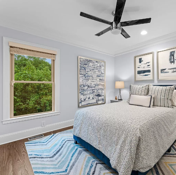 Bedroom with bed, blue rug, and large window overlooking trees.