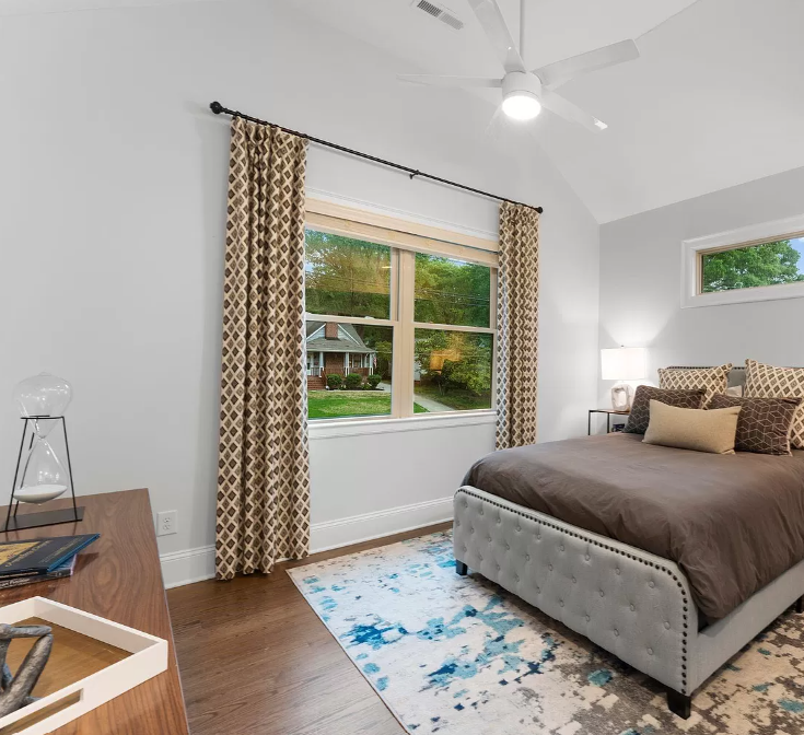 Bedroom with bed, window, patterned curtains, and wooden dresser.
