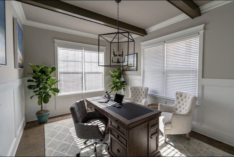 Office with desk, chairs, plants, windows, and a large geometric chandelier.  Neutral tones, sunny light.