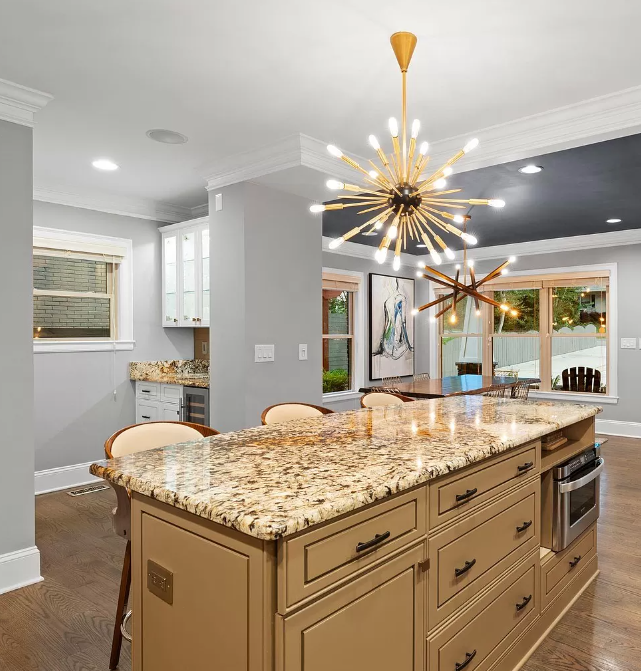 Kitchen island with granite countertop, gold chandelier, cabinetry.