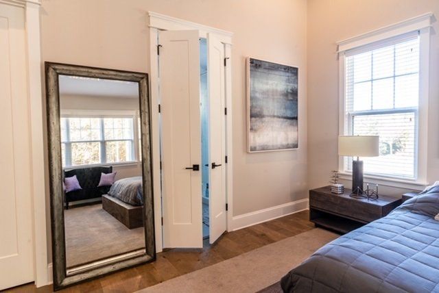 Bedroom with a large mirror, open white door, abstract art, and a window. Beige walls and wood floors.