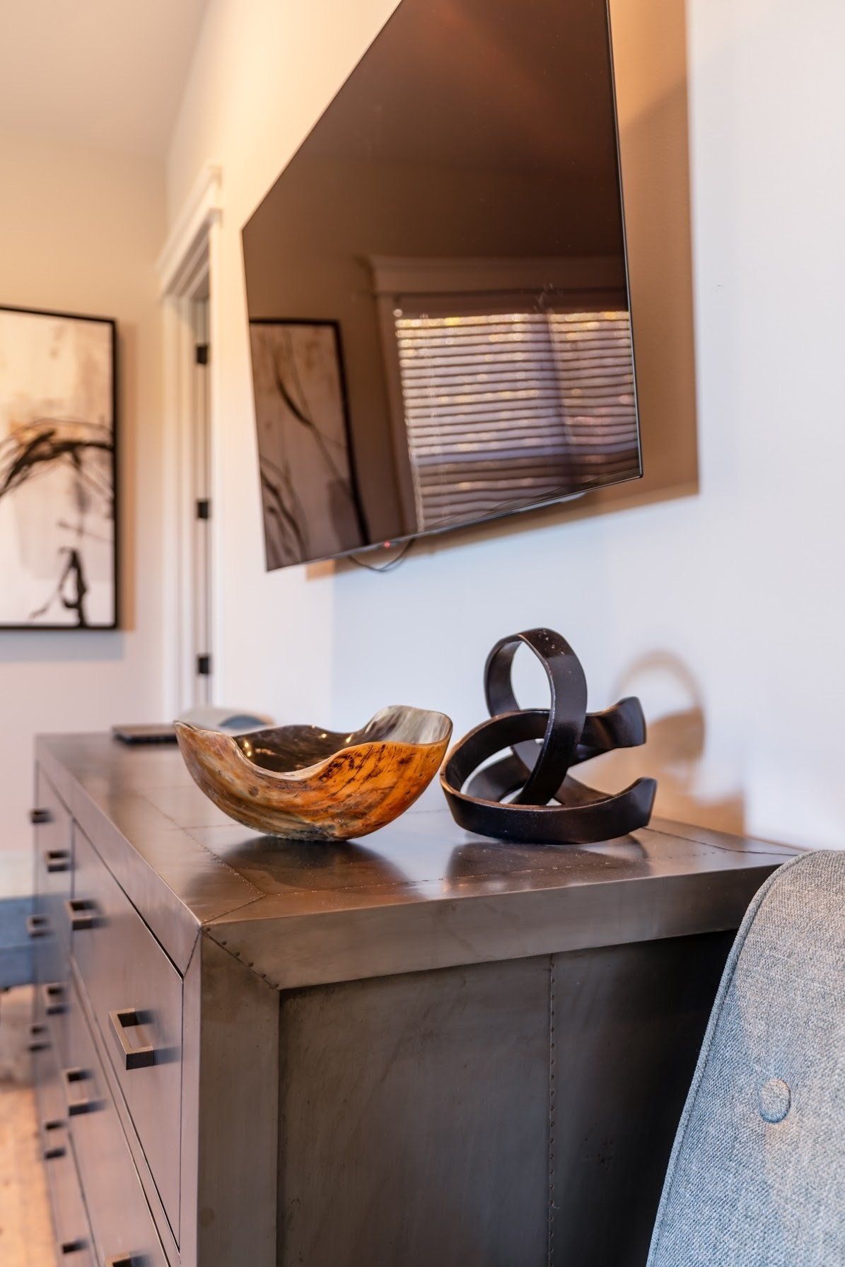 Wooden bowl and metal sculpture on a dark dresser under a mounted TV.