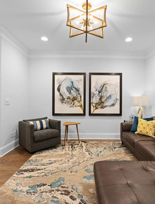 Living room with brown leather sofa, two abstract paintings, and a patterned rug.